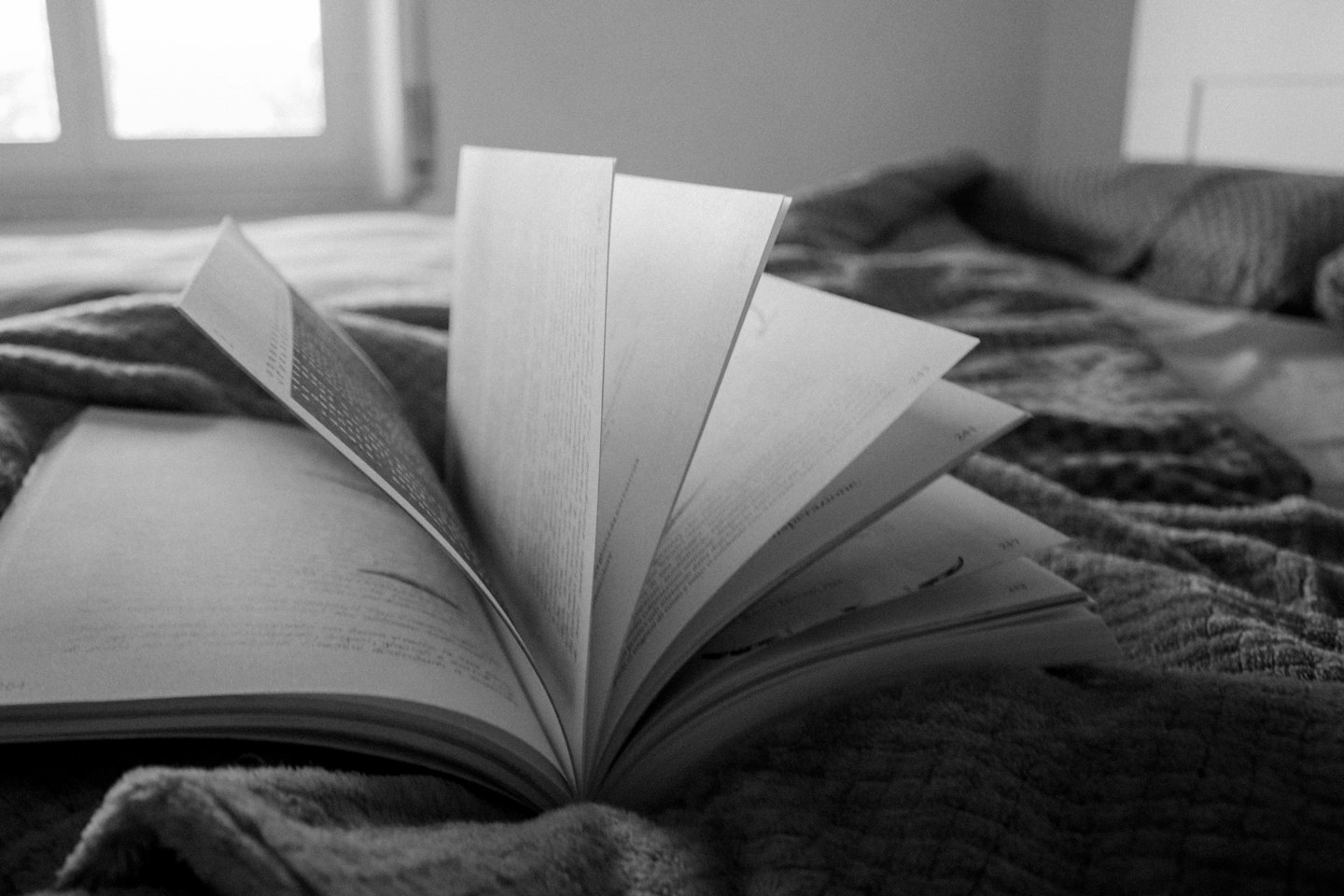 Open book with fanned pages on a patterned blanket.