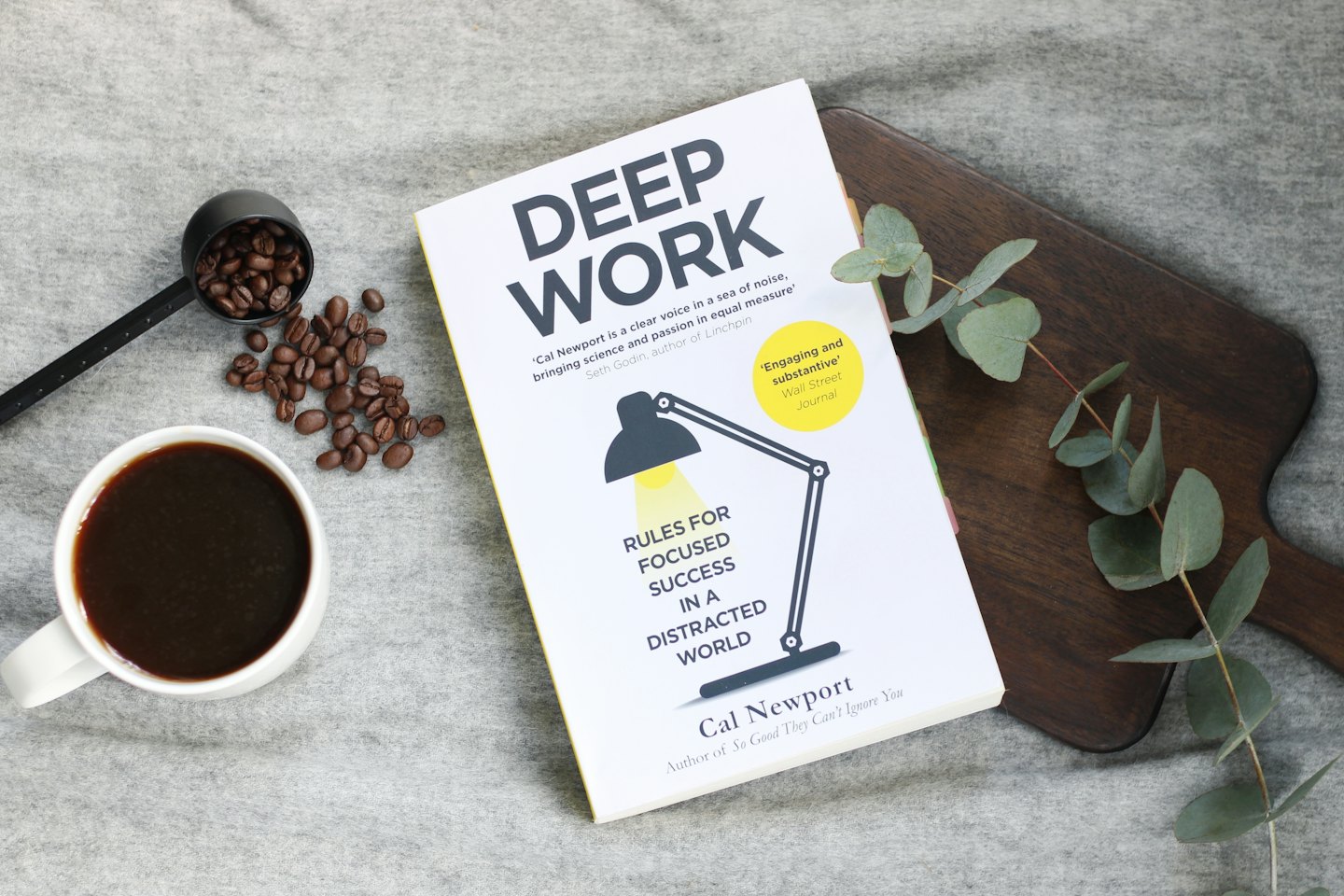 Book 'Deep Work' with coffee and eucalyptus on a wooden board.